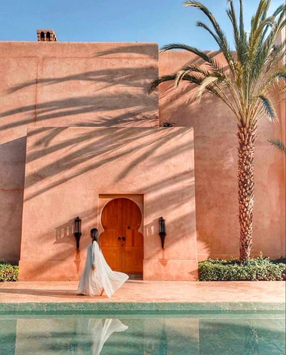 Façade de palais marocain en terre cuite, porte sculptée, palmier et reflet dans une piscine